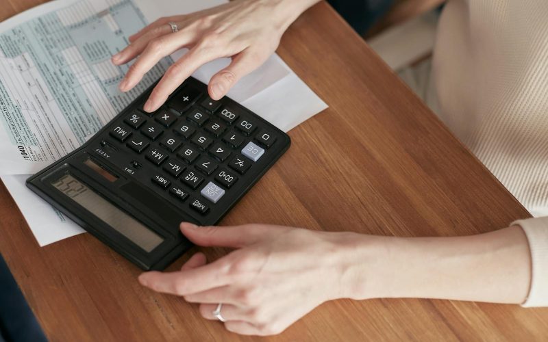 Close-up of a woman using a calculator and reviewing bills at home.
